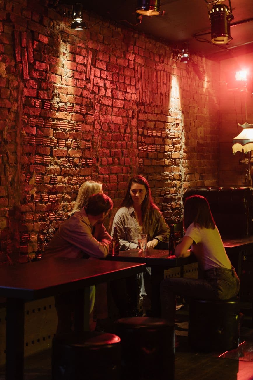Friends enjoying a casual drink in a warm, atmospheric bar setting with exposed brick walls.