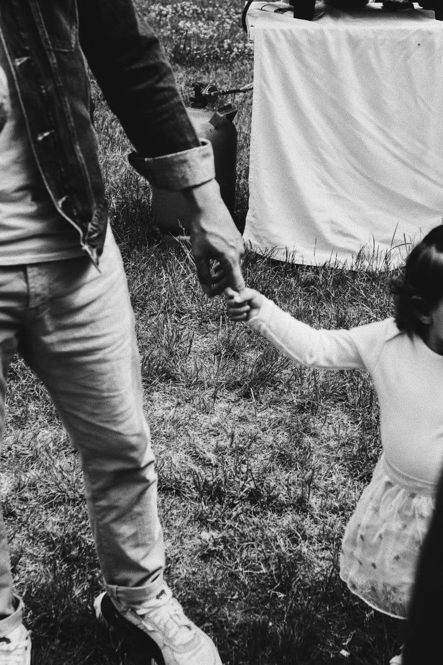 Black and white photo of father holding daughter's hand in Berlin park, showcasing parent-child bond.