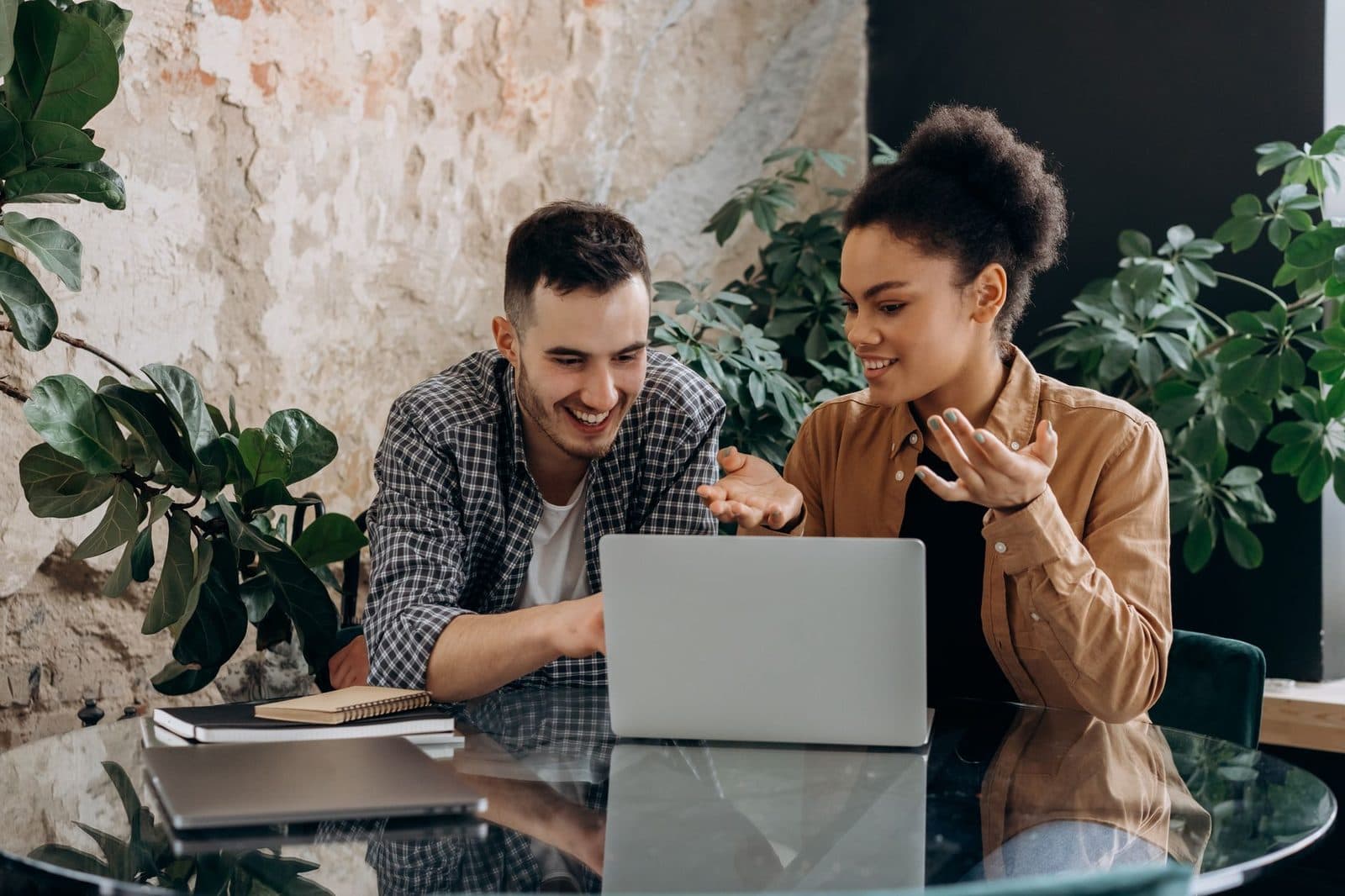 Two colleagues collaborating on a laptop in a modern workspace with plants.