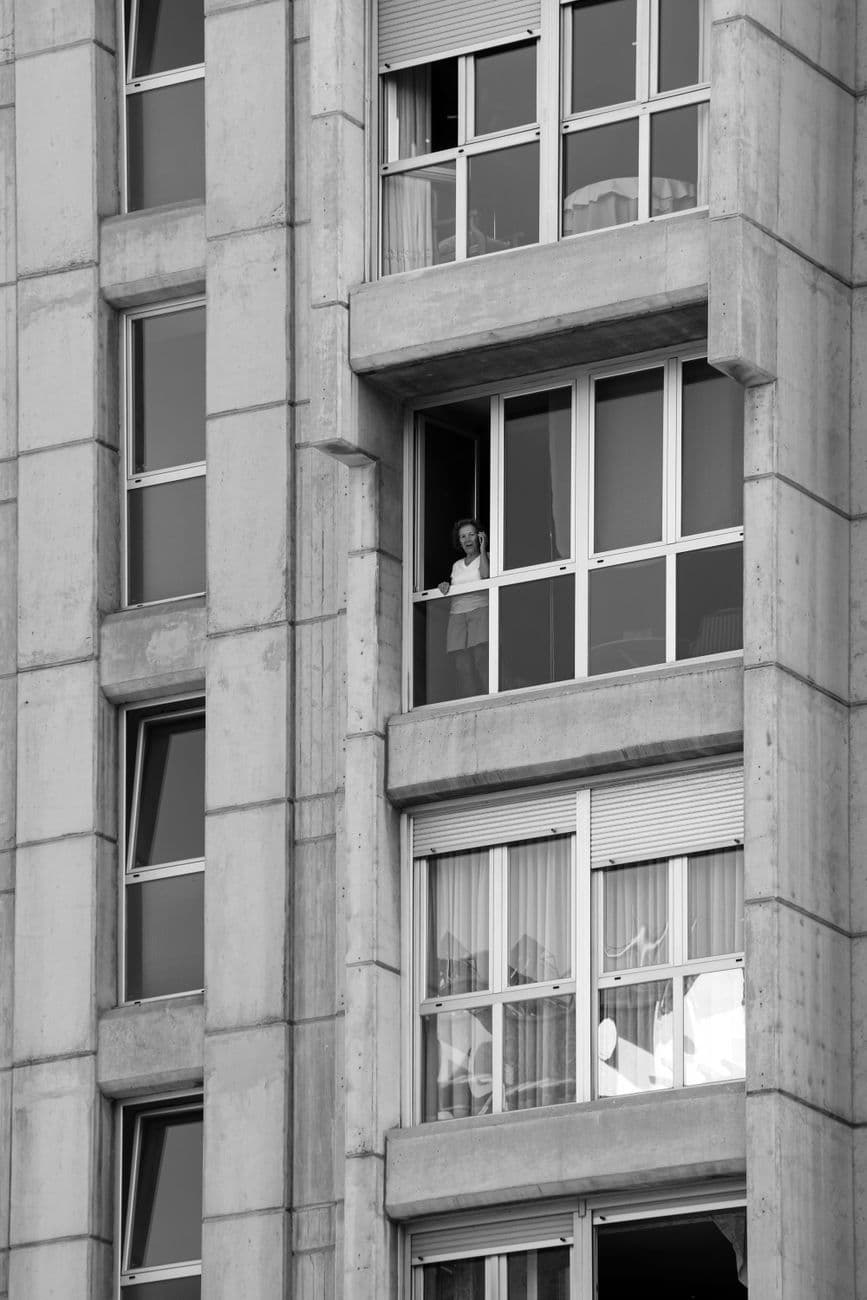 A person looking out from a high-rise building window in a cityscape. Urban lifestyle captured in monochrome.