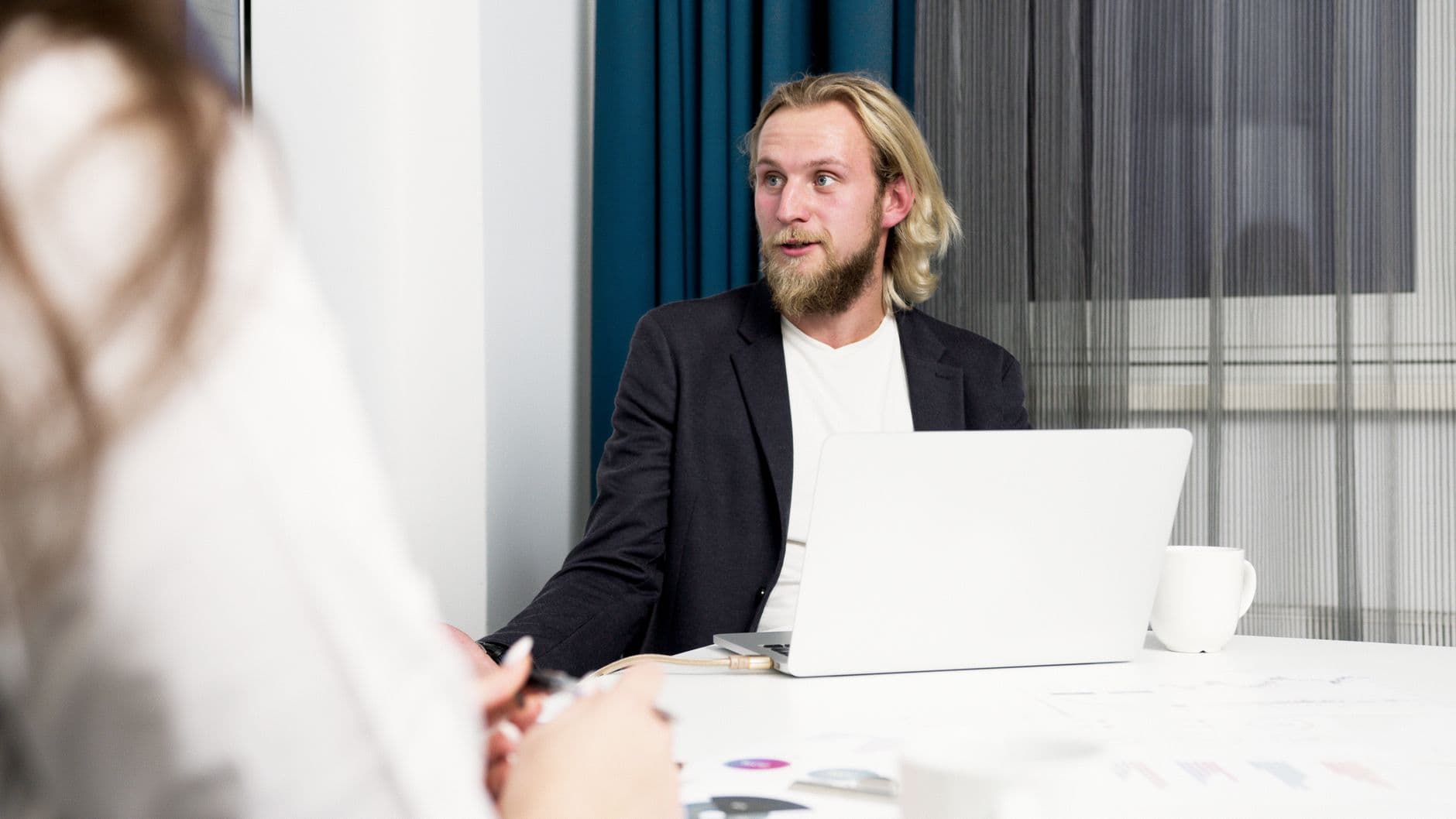 A bearded businessman engaged in a discussion at an office with a laptop.