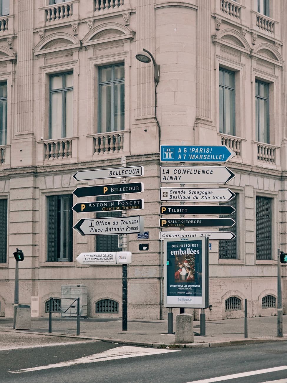 Signs directing to notable locations in Lyon, France, with an elegant building in the backdrop.