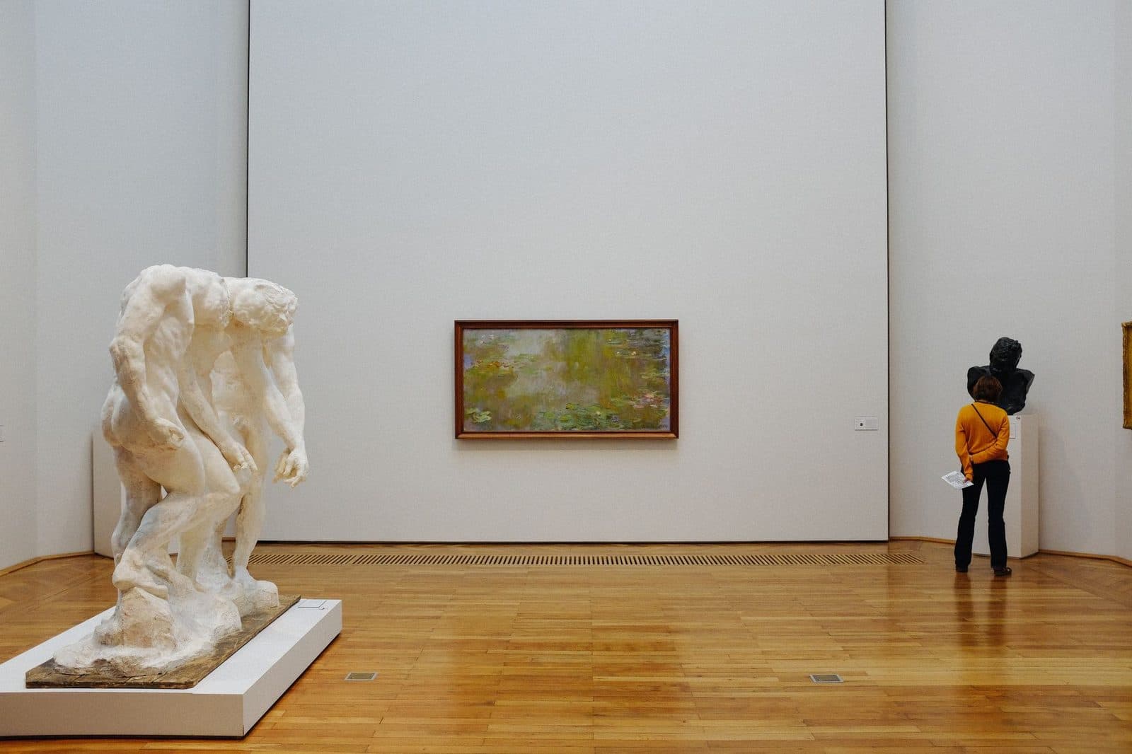A person admires art in a modern gallery featuring sculpture and painting.