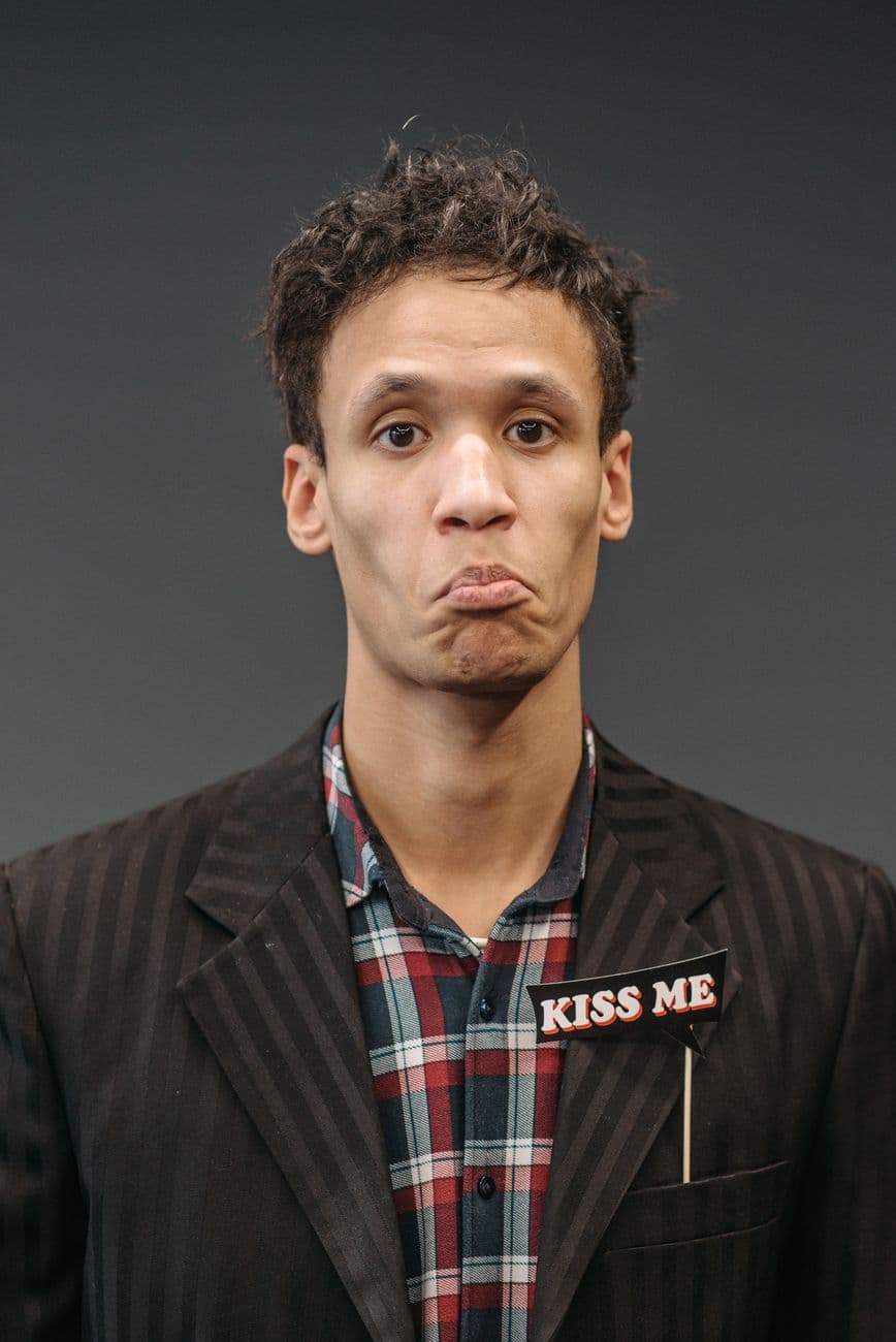 Man in formal attire with a cute pout and 'Kiss Me' badge, expressive portrait.
