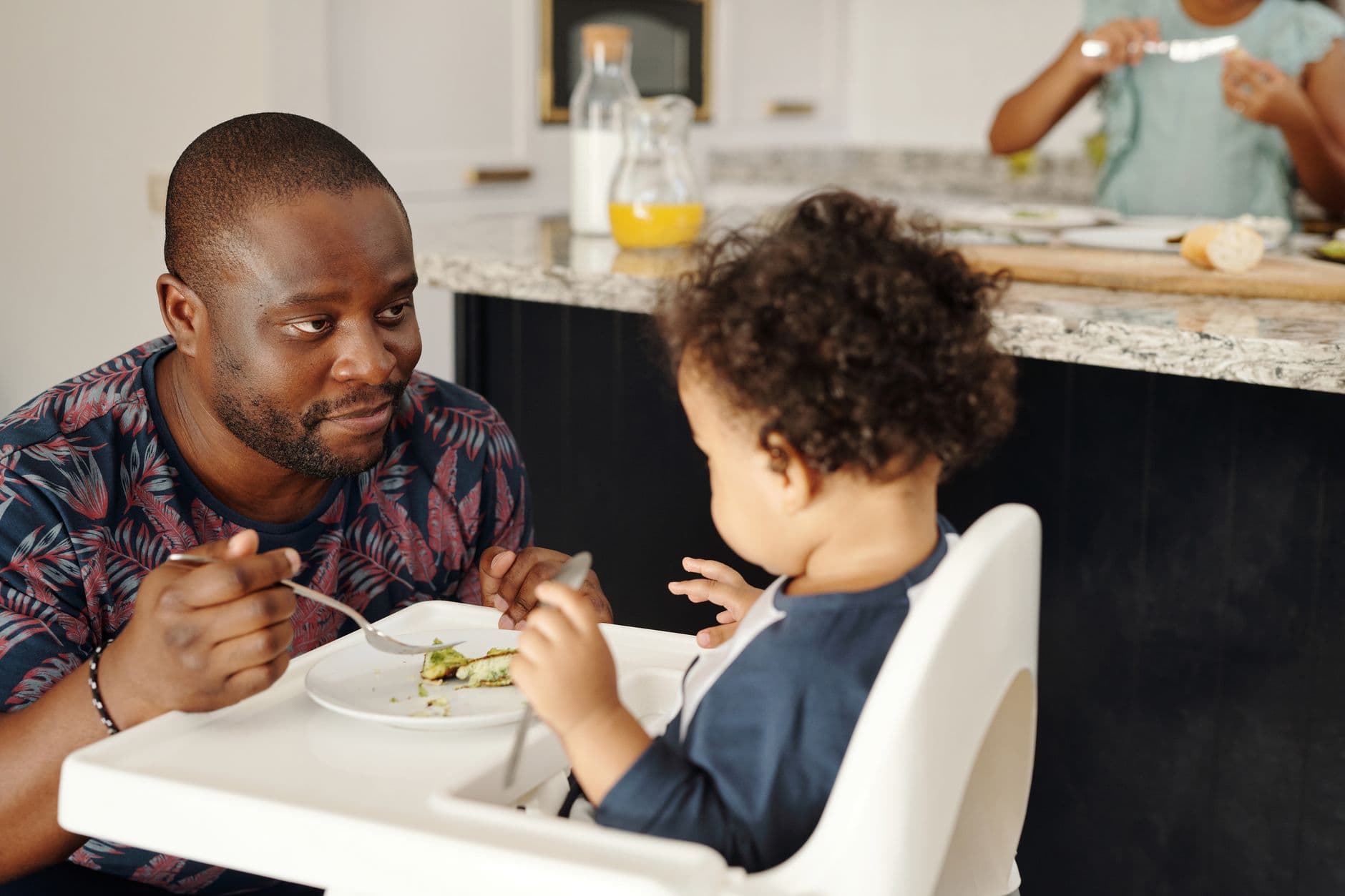 A father shares a meal with his young child in the kitchen, capturing a tender family moment.