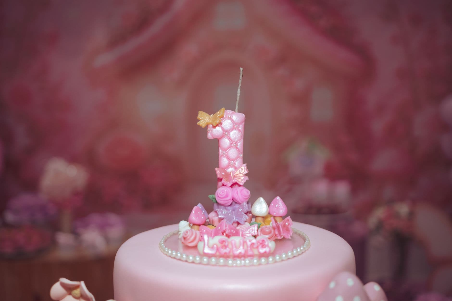 A close-up of a pink decorated first birthday cake with a number one candle.