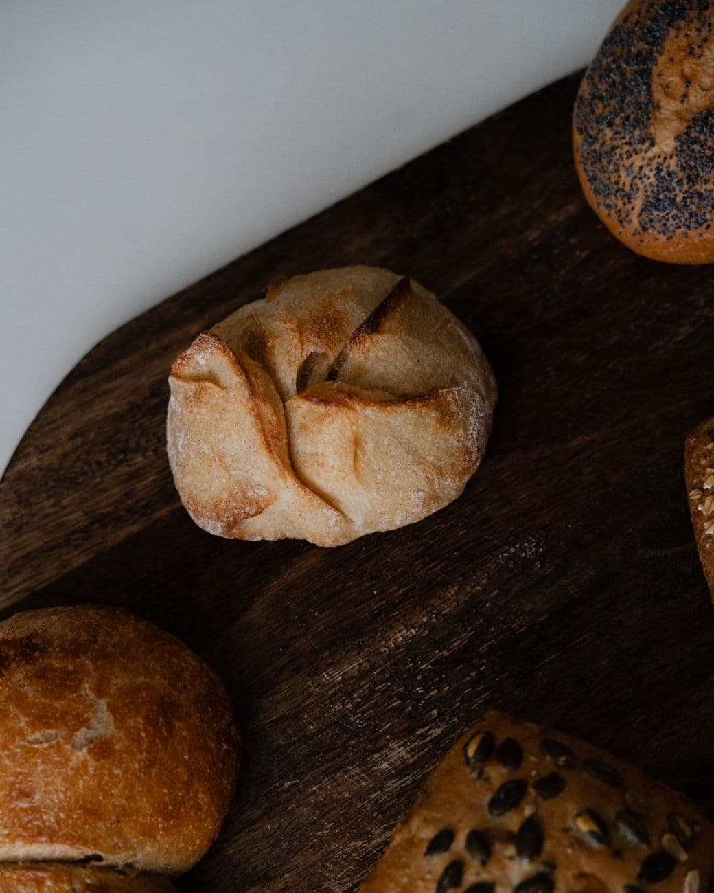 A beautifully arranged assortment of artisan bread rolls on a dark wooden board.