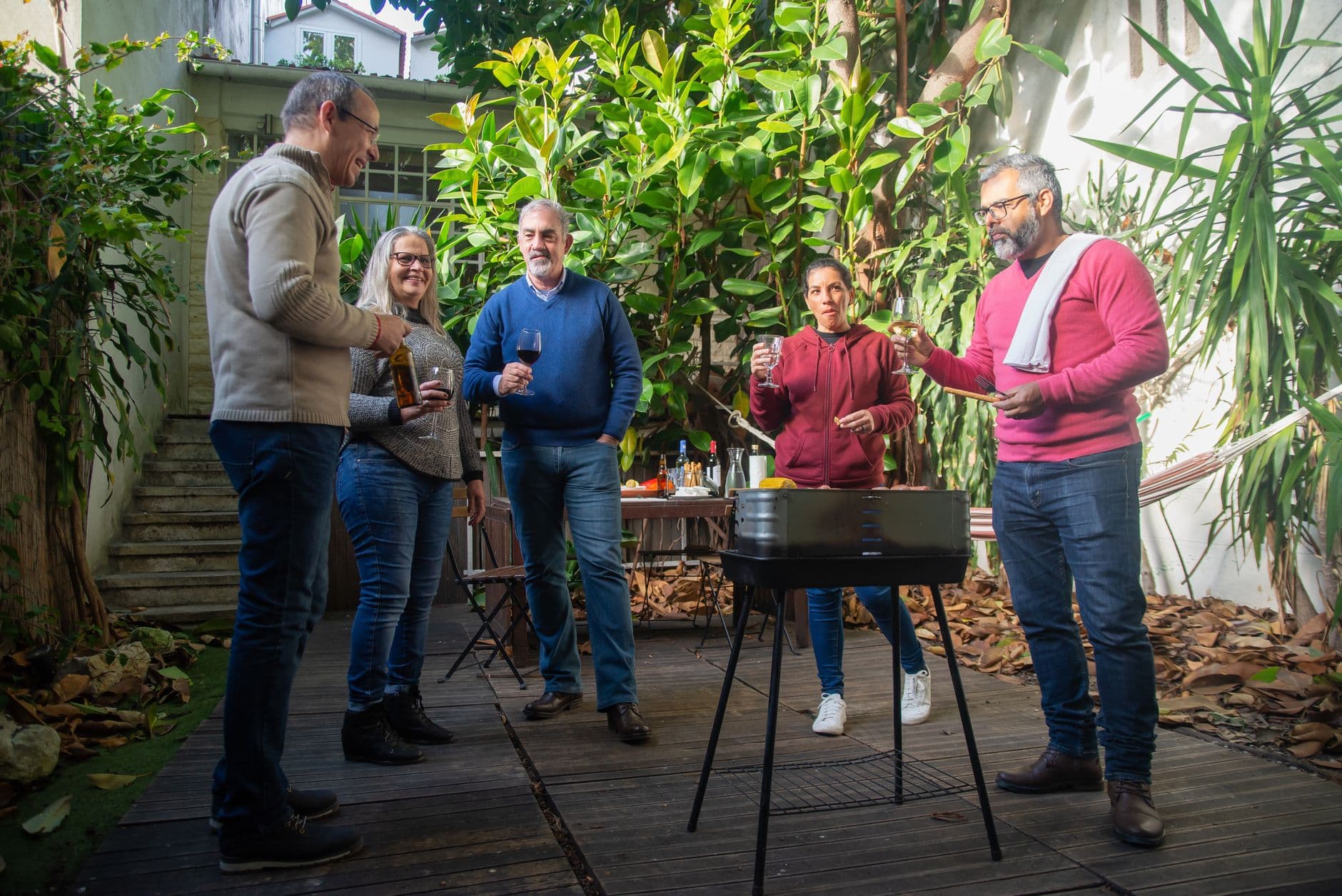 A lively gathering of adults enjoying a barbecue and drinks in a Portuguese garden.