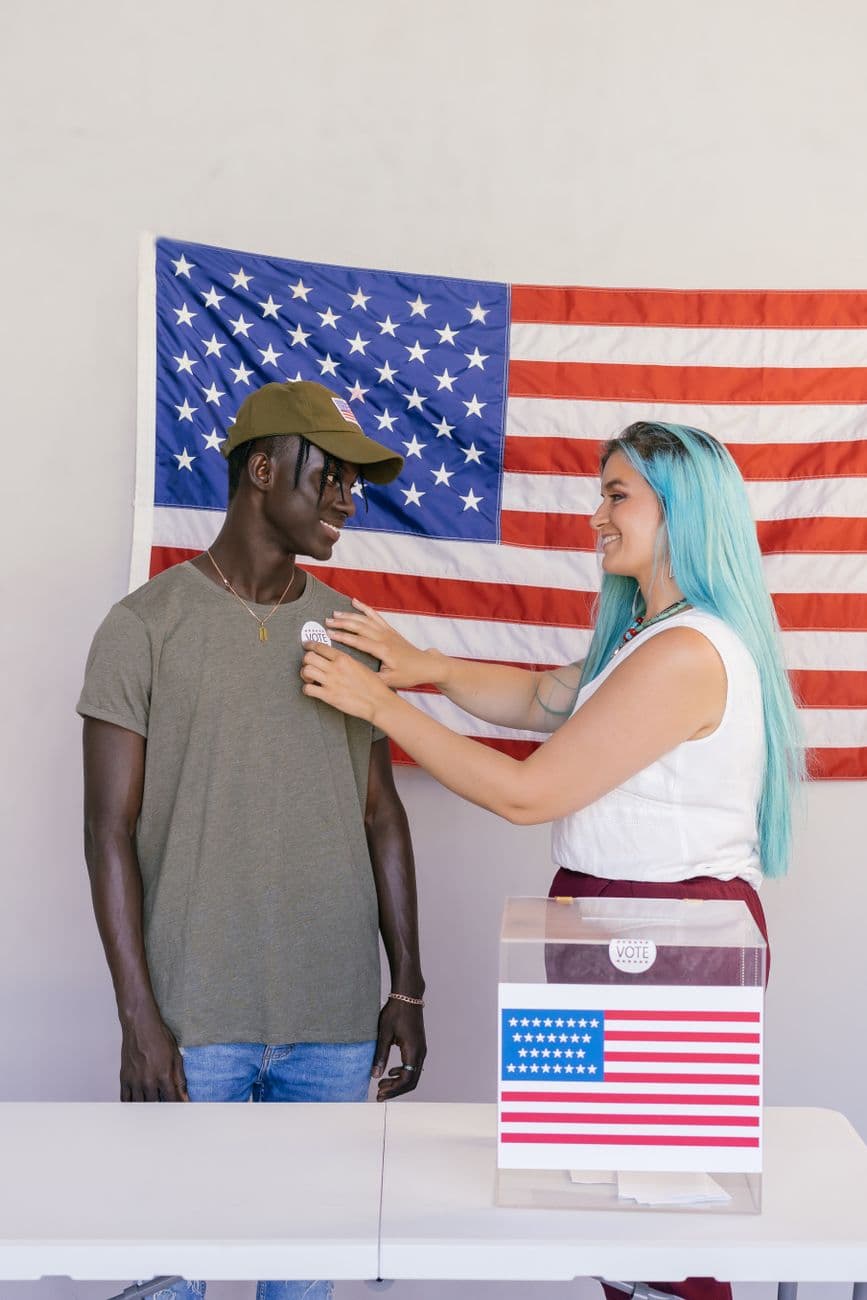 Two diverse voters at a polling station with the American flag.
