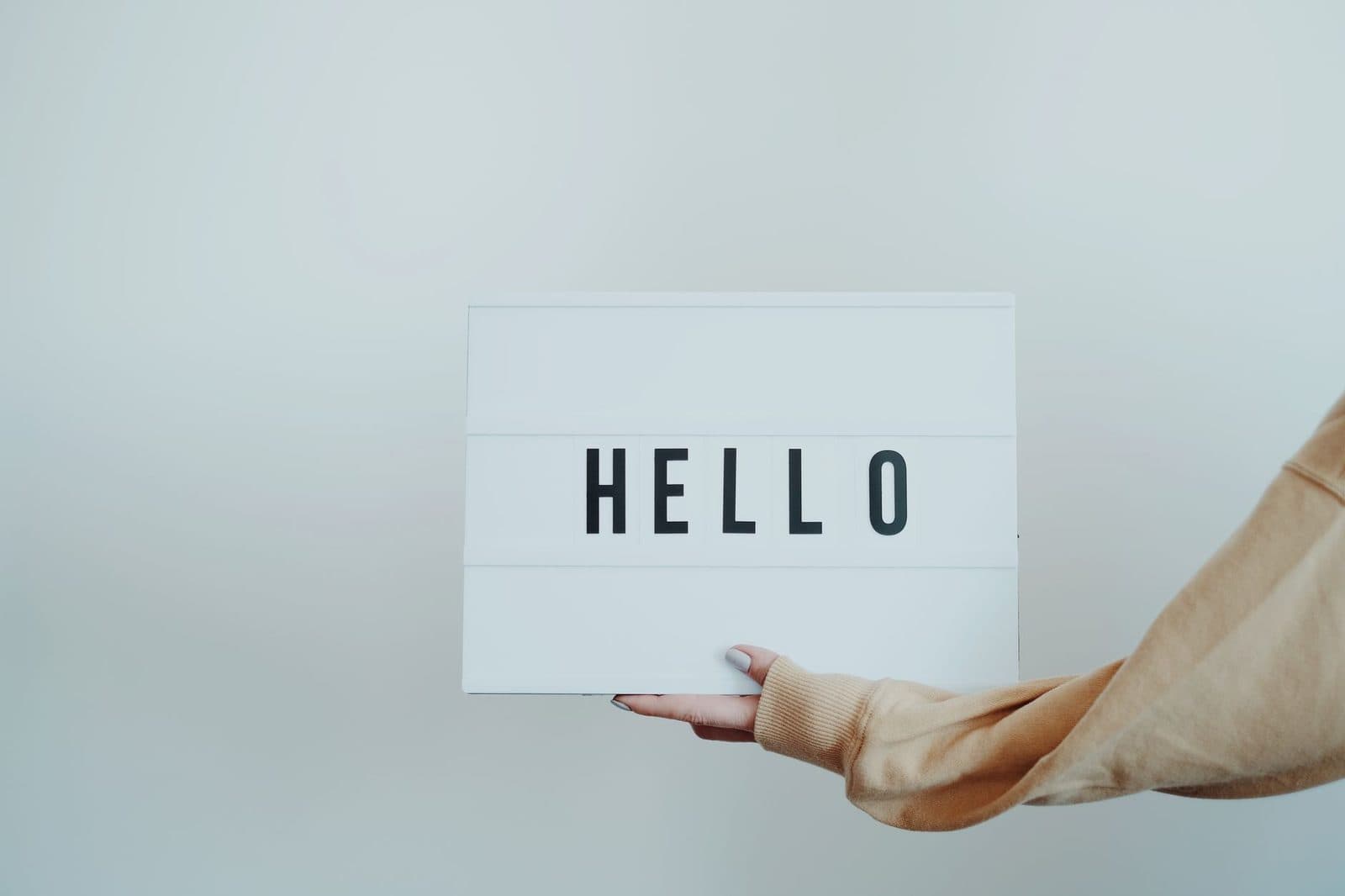 A hand holds a white sign displaying the word 'Hello' against a plain background.
