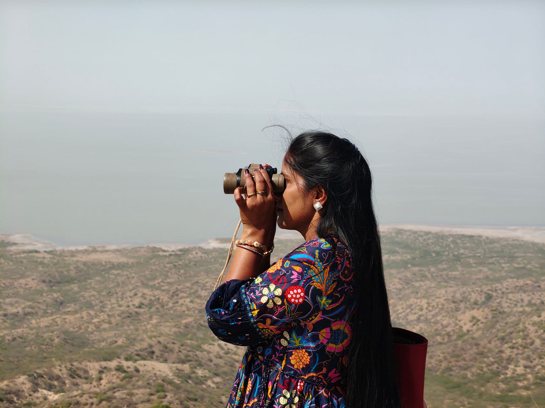 Woman using binoculars to observe distant landscape from an elevated point.