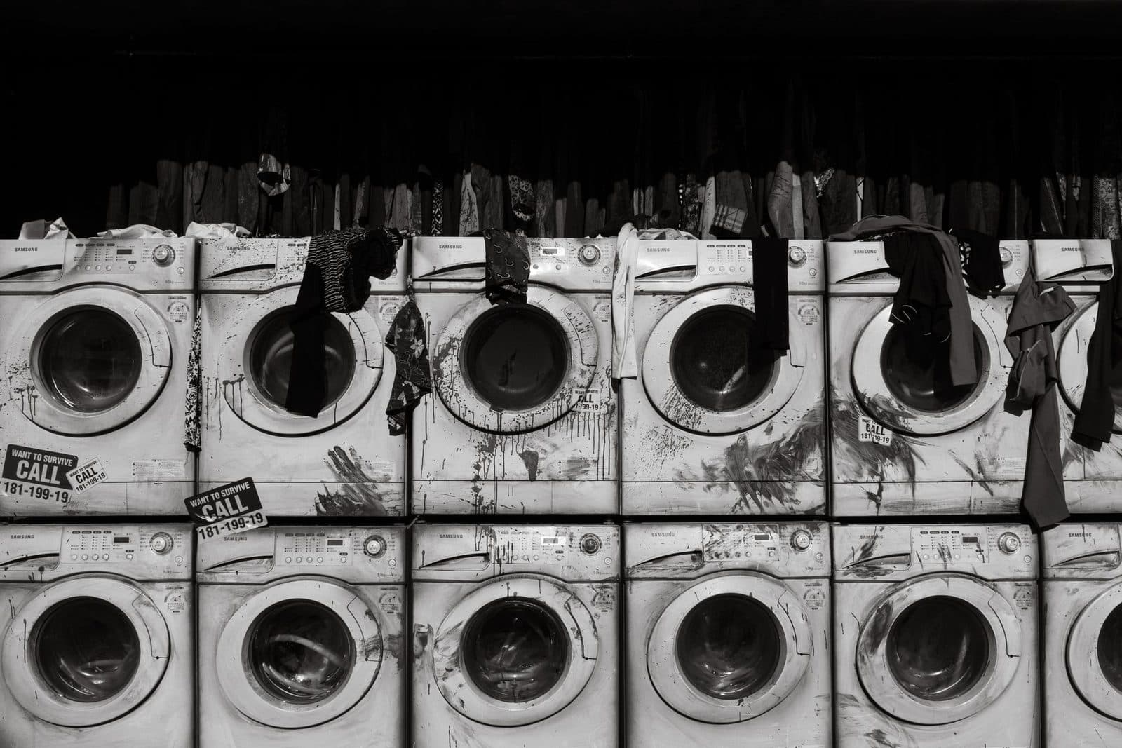 Grungy industrial washing machines lined up with clothing, creating a dramatic monochrome scene.