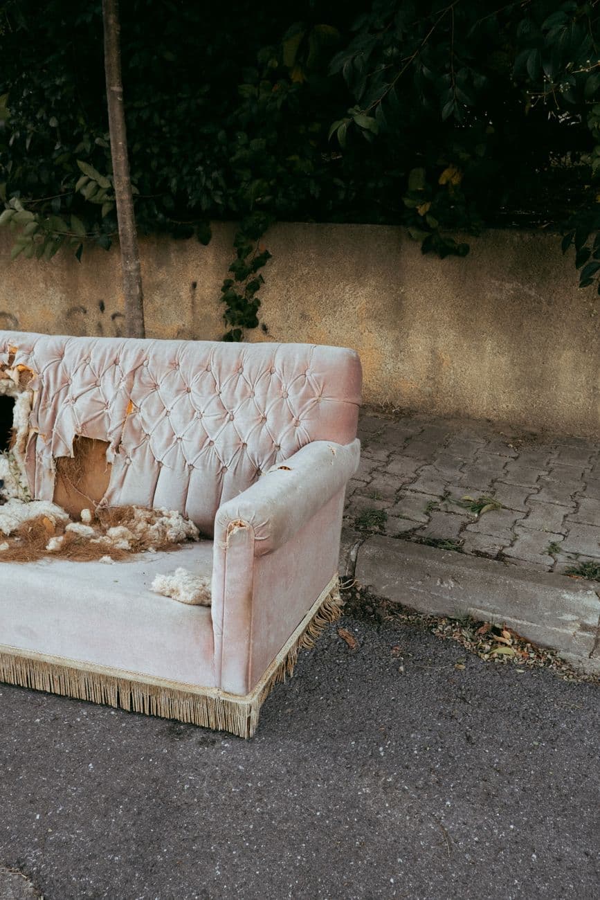 A worn-out sofa sits abandoned on a city street, highlighting urban decay.