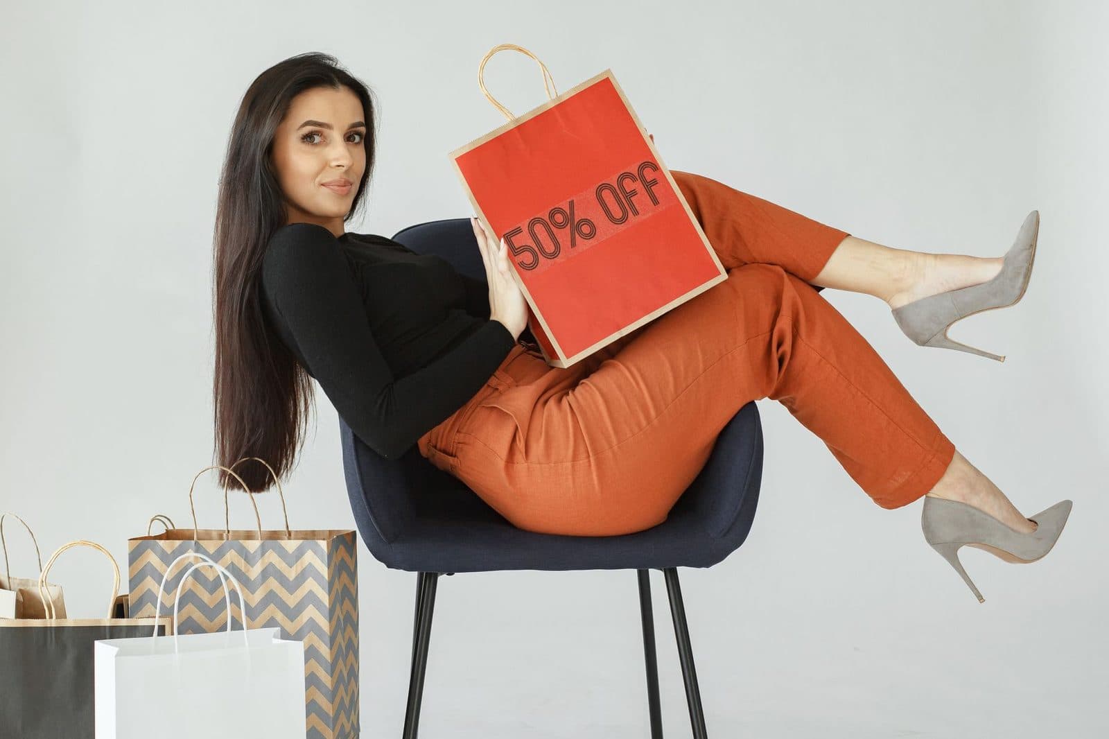Stylish woman in chic pose holding a 50% off shopping bag, surrounded by bags.