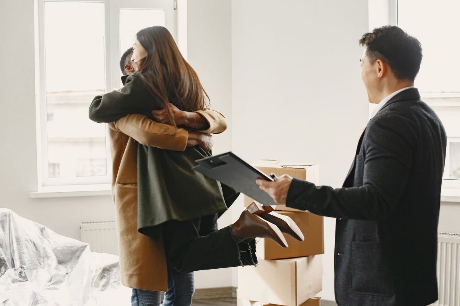 Joyful couple embracing as they move into new home, assisted by friendly realtor.