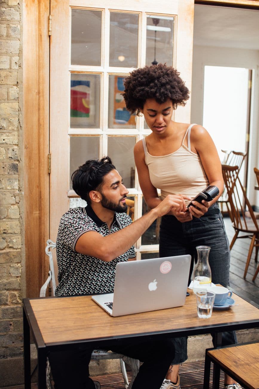Man and woman in conversation at a coffee shop managing payment using a terminal device.