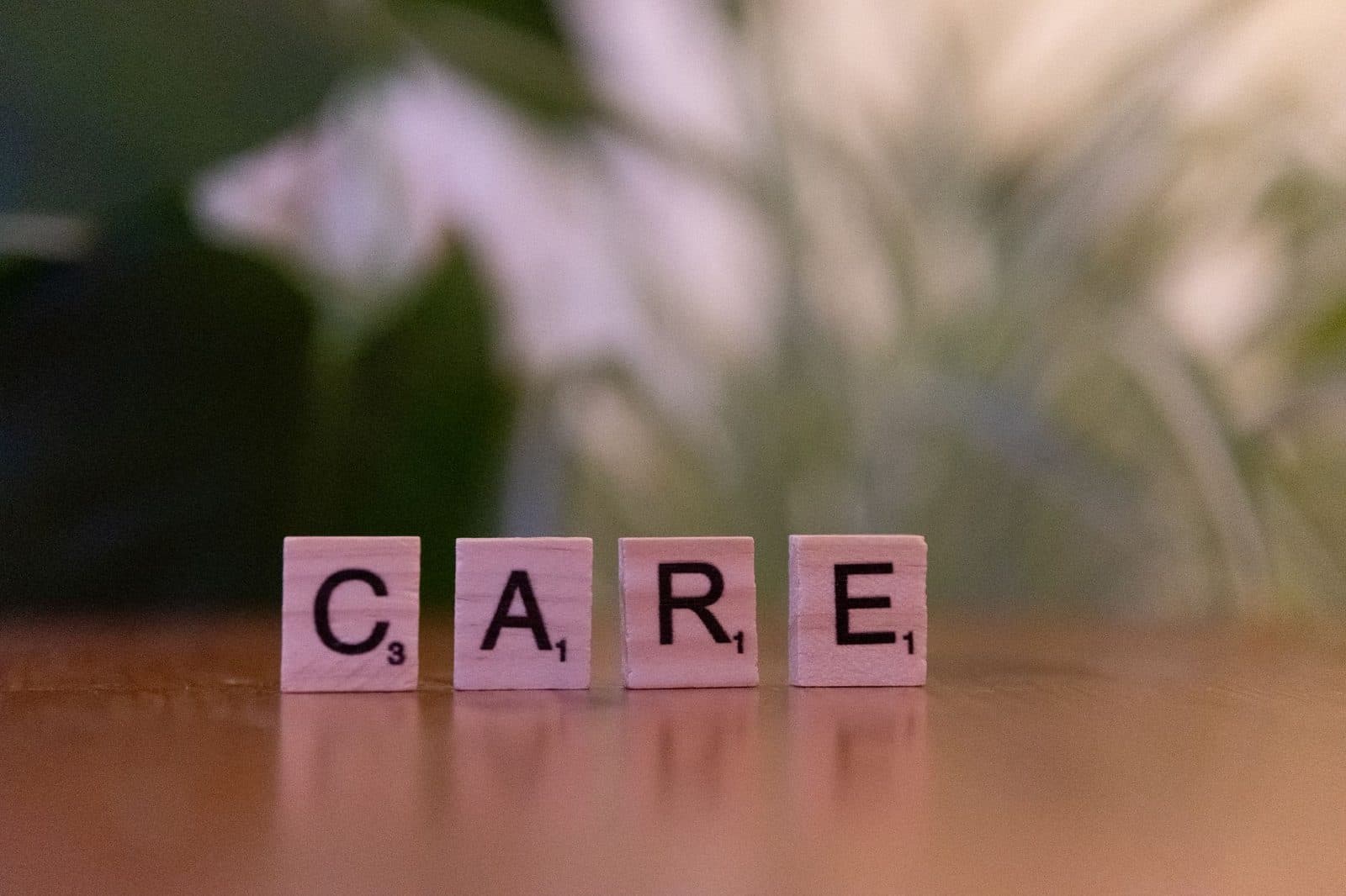Close-up of wooden tiles spelling 'CARE' on a table with a blurred background, evoking a sense of support.