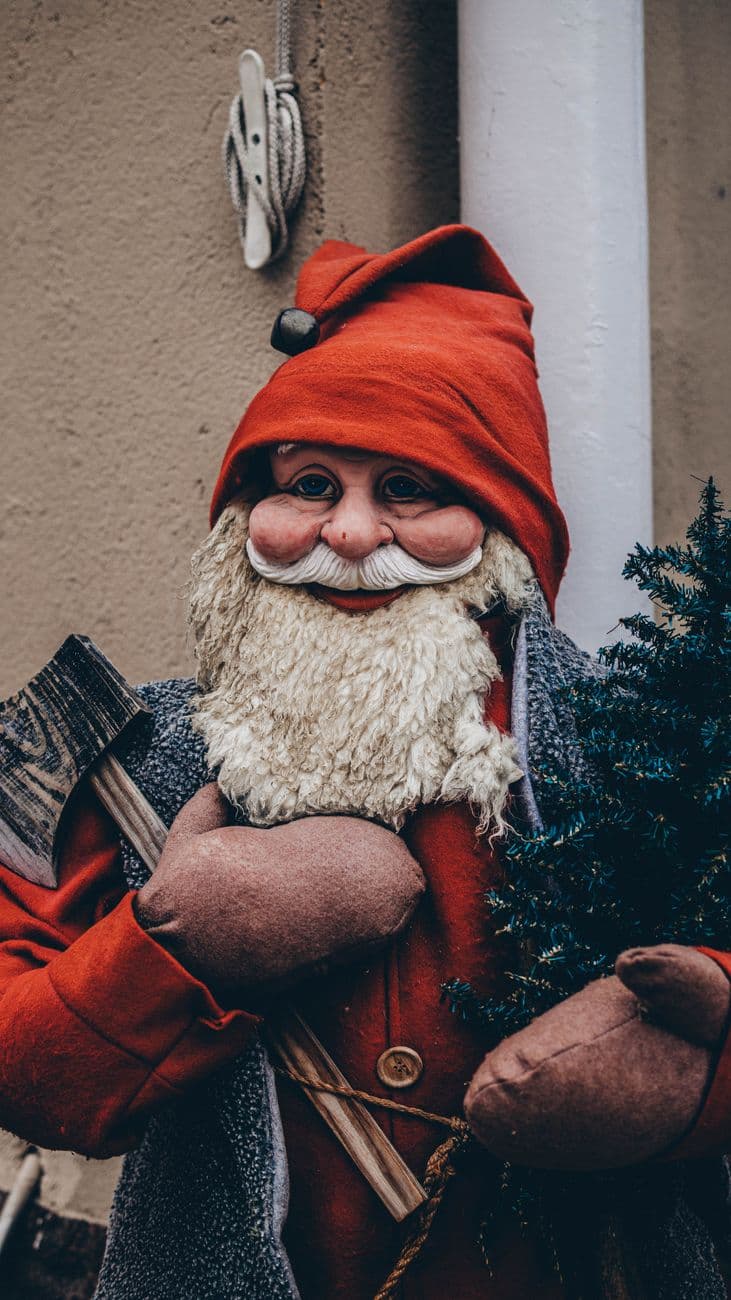 A charming Santa Claus figurine with axe and tree evokes holiday cheer and warmth in a winter setting.