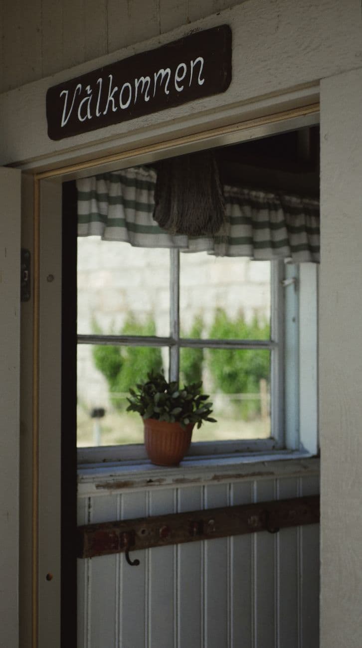 Charming entrance with a welcoming sign and window view of a plant.