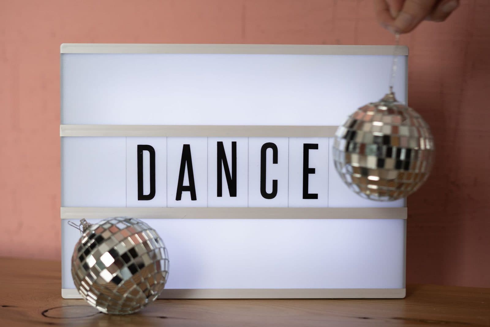 A lightbox displaying the word 'DANCE' with shiny disco balls on a wooden surface.