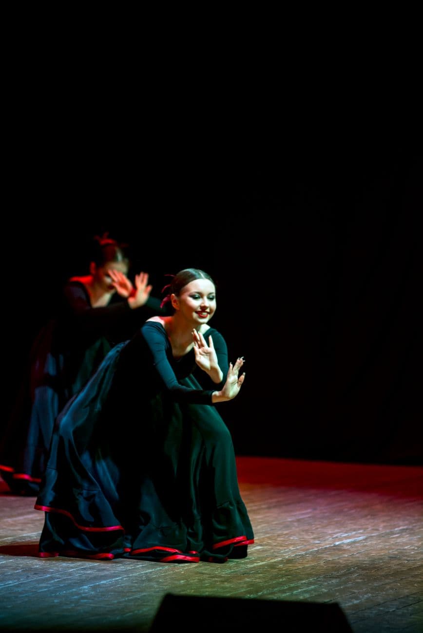 A graceful dancer performing in a black dress during a folk dance show on stage.