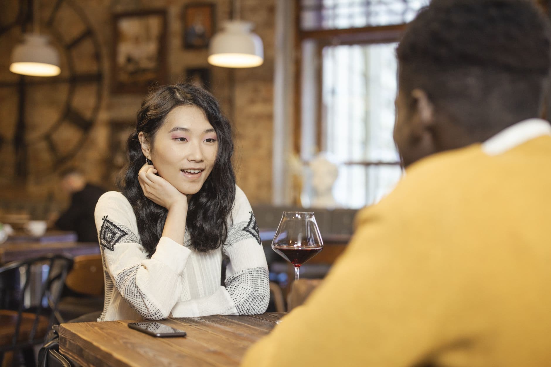Two adults enjoying a conversation over wine in a warm, cozy café atmosphere.