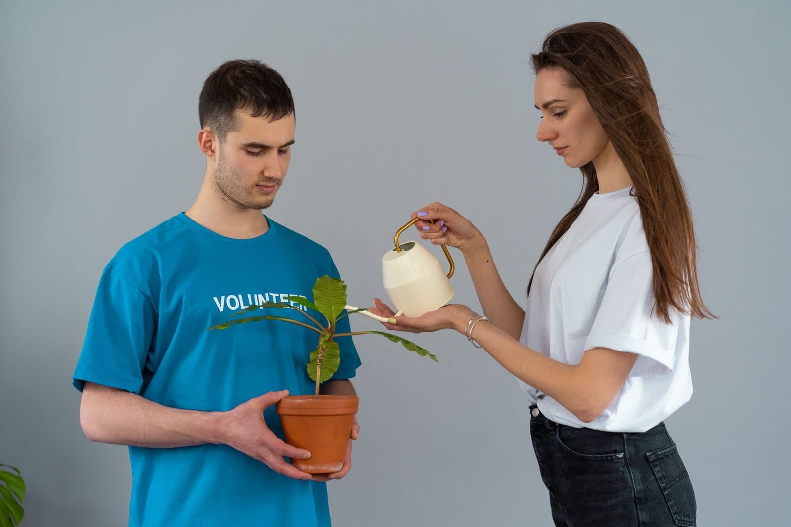 Two young volunteers nurturing a potted plant. Man holding, woman watering.