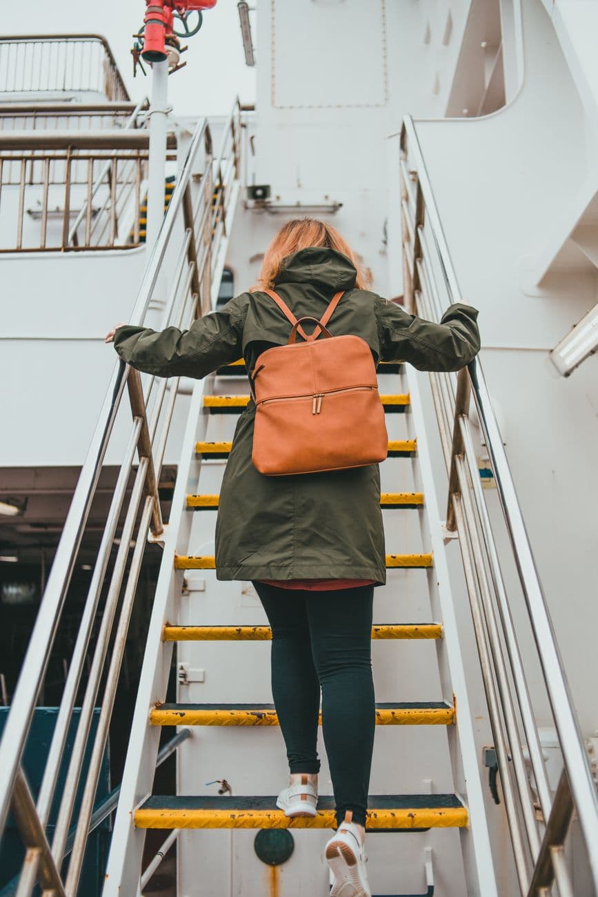 A woman with a backpack ascends stairs on a ferry deck, emphasizing travel and exploration.