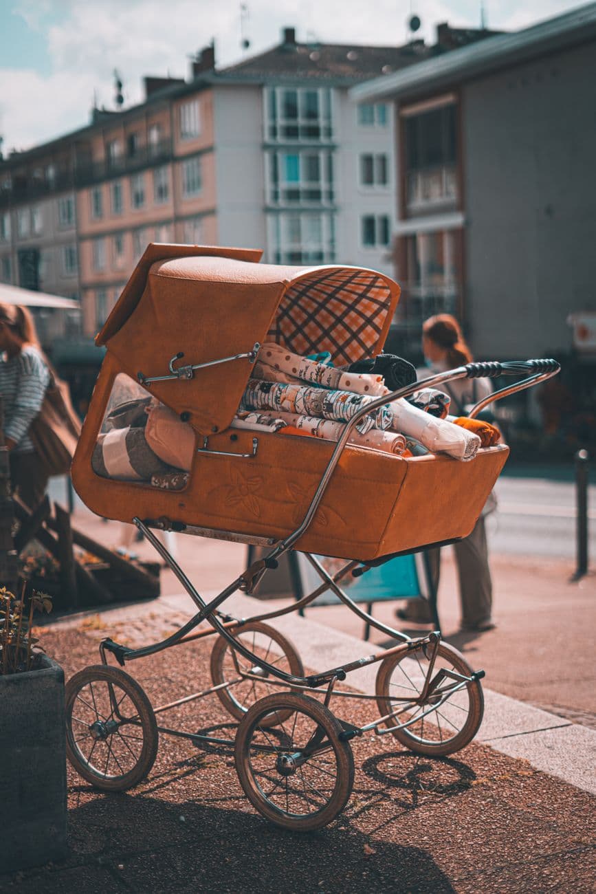 A classic brown baby stroller parked on a city sidewalk, conveying nostalgia.