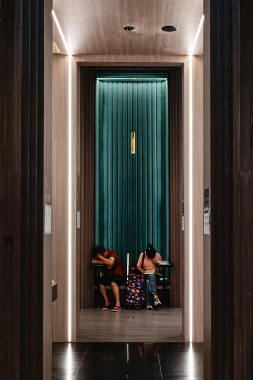 Two people seated in a modern hotel lobby near an elevator entrance.