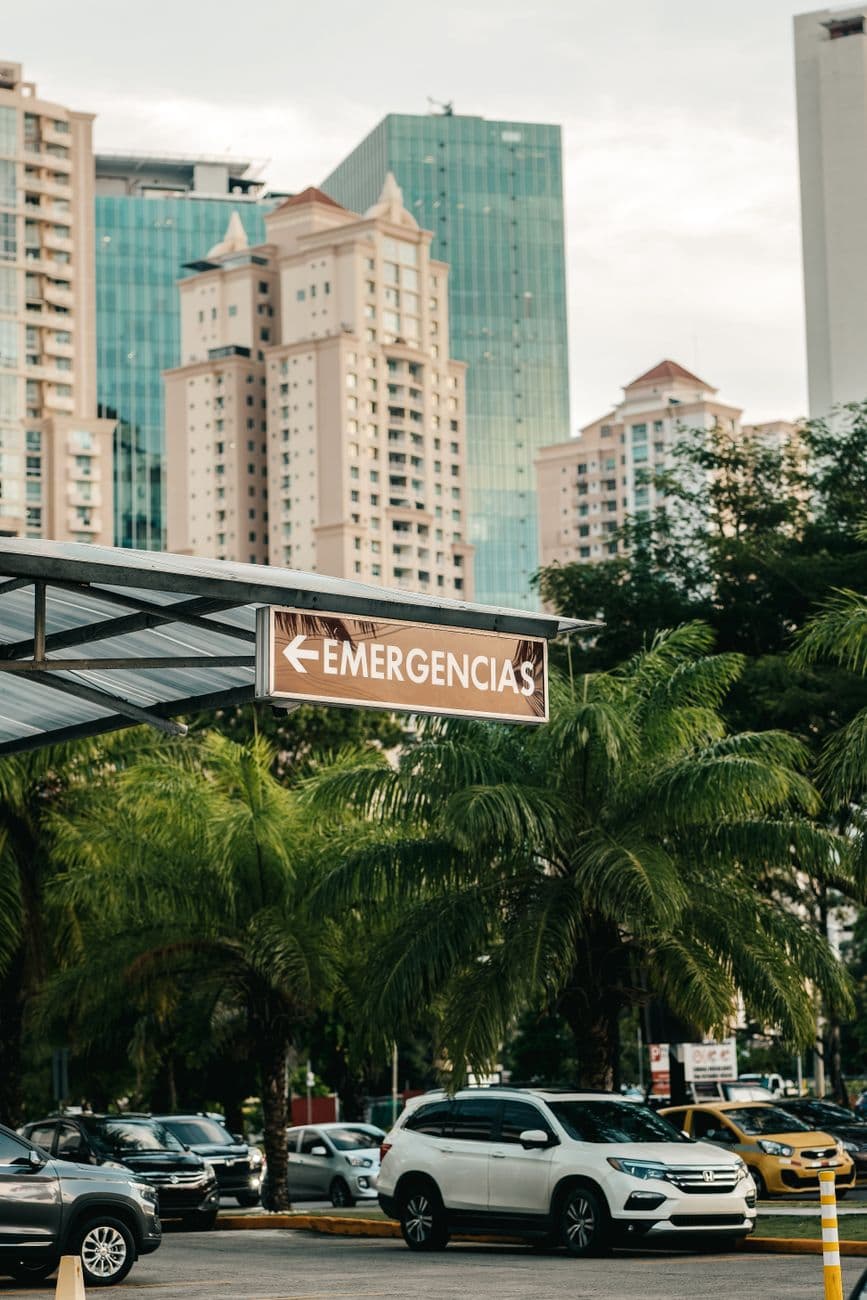 Vertical shot of cityscape featuring high-rise buildings, parked cars, and an emergency sign.