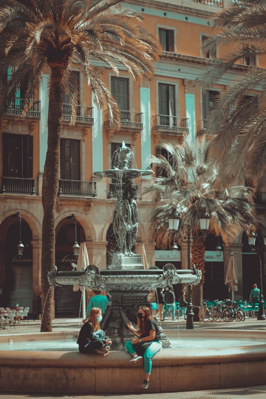 People enjoying a sunny day at the iconic Placa Reial fountain in Barcelona, Spain.