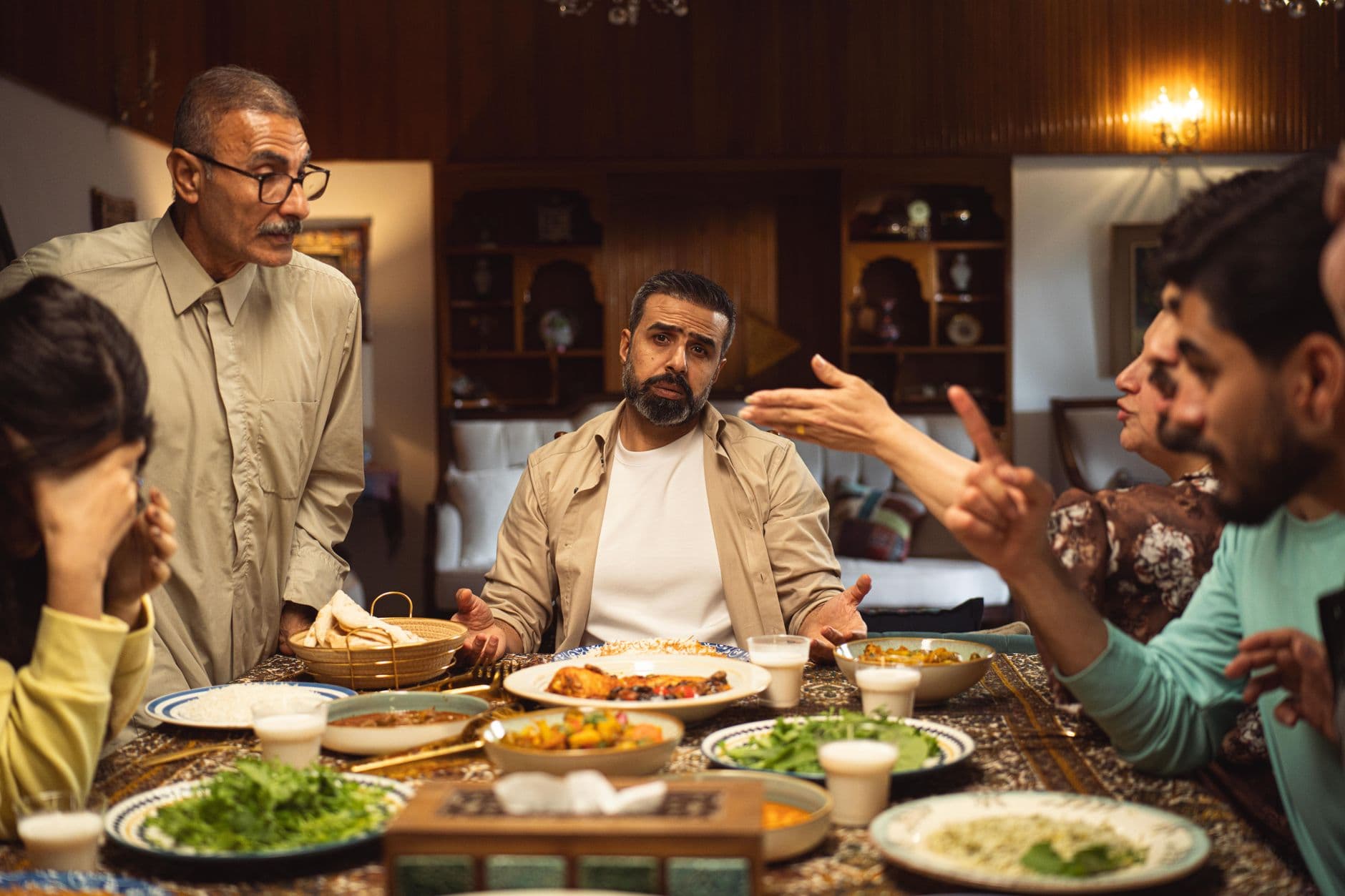 A family engages in a lively discussion around a dinner table filled with dishes.