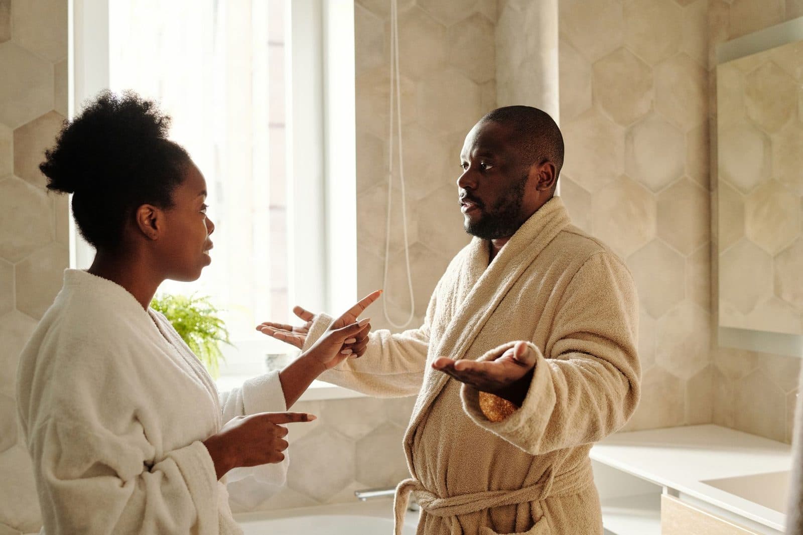 A couple in bathrobes having a discussion in a bathroom setting, expressing emotions.