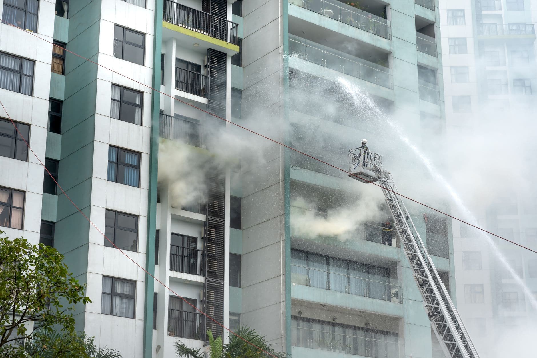Firefighters on a ladder battling a fire in an urban residential high-rise.