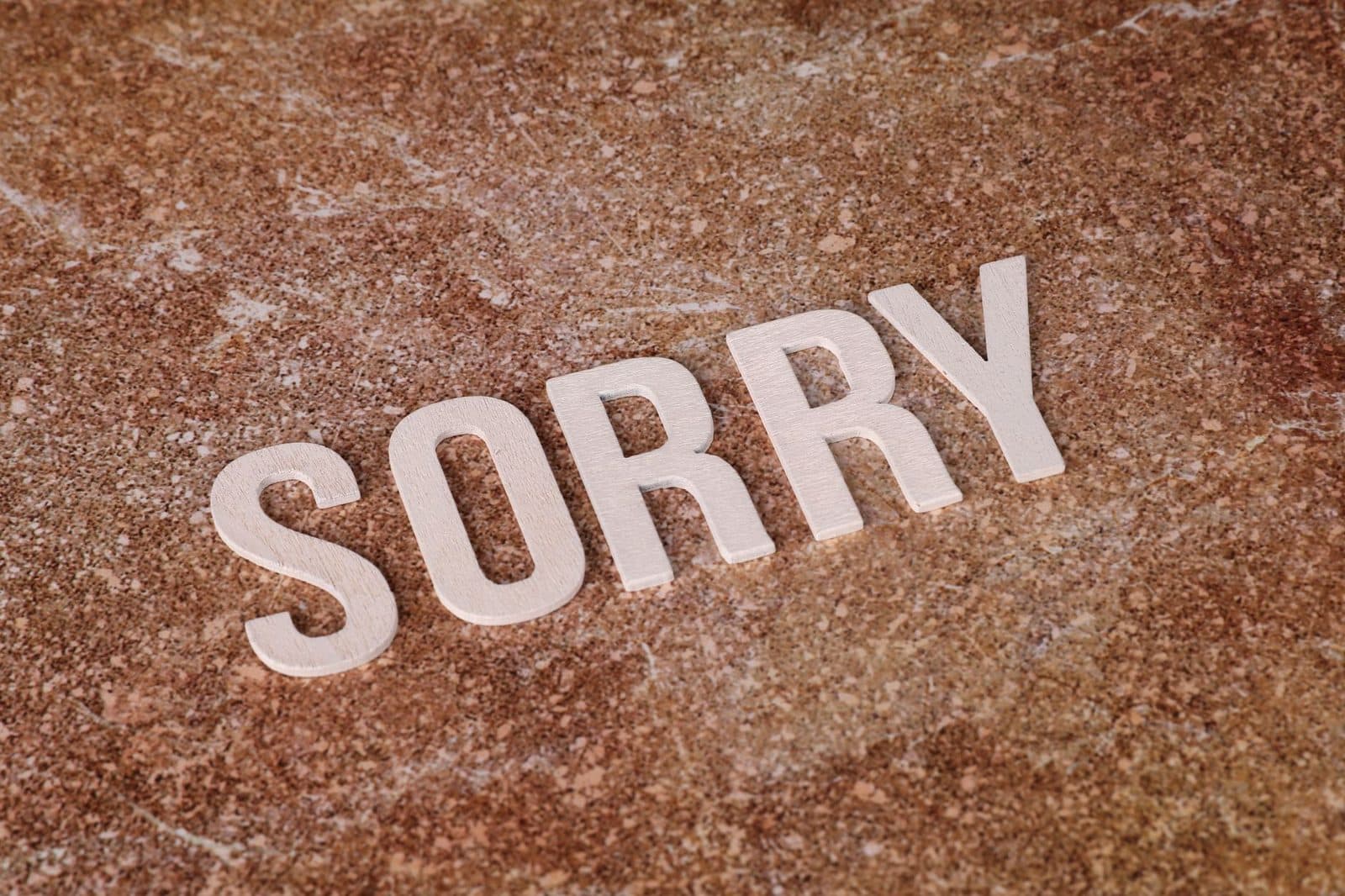 Wooden letters spelling 'SORRY' on a textured marble surface, symbolizing apology or regret.