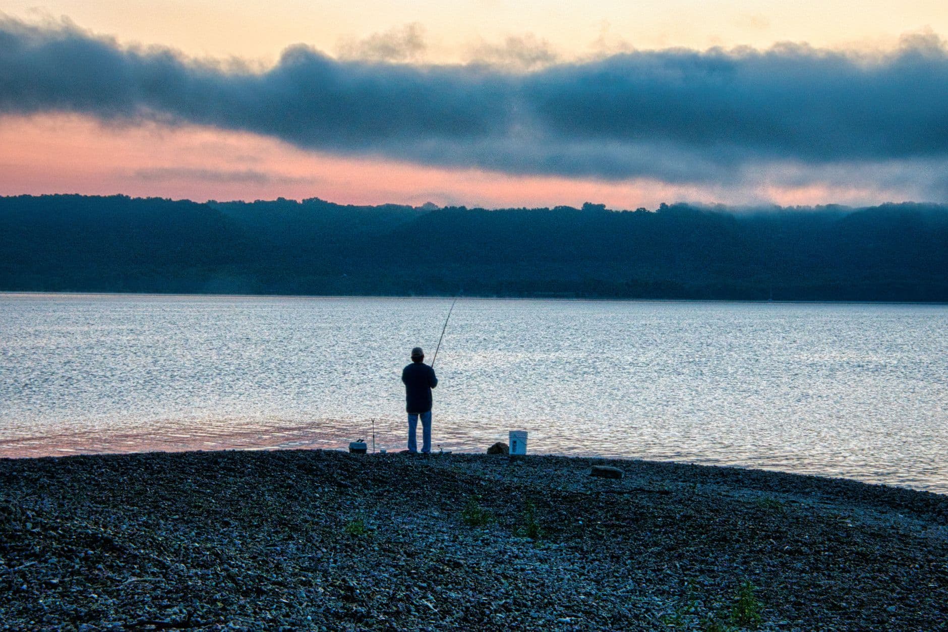 A lone fisherman at sunrise on the serene shores of Lake City, MN, casting a line into the tranquil waters.