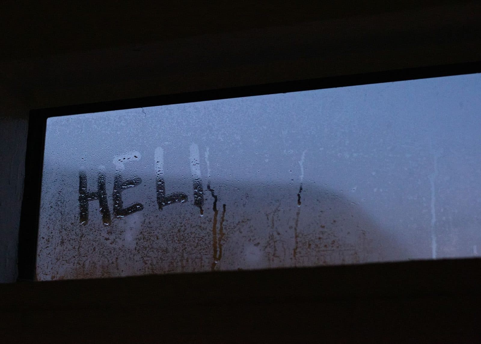 Steamy window with 'HEL' written on it, captured during twilight, enhancing the mysterious vibe.