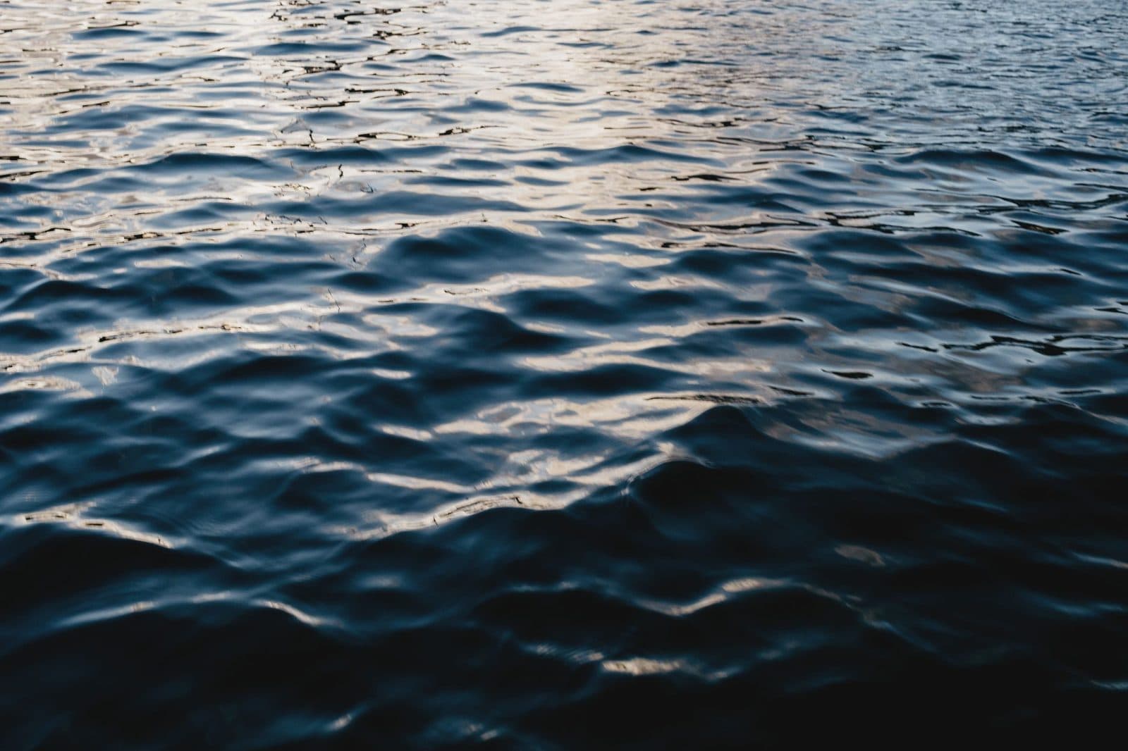 From above of rippling blue water of ocean illuminated by light in daytime