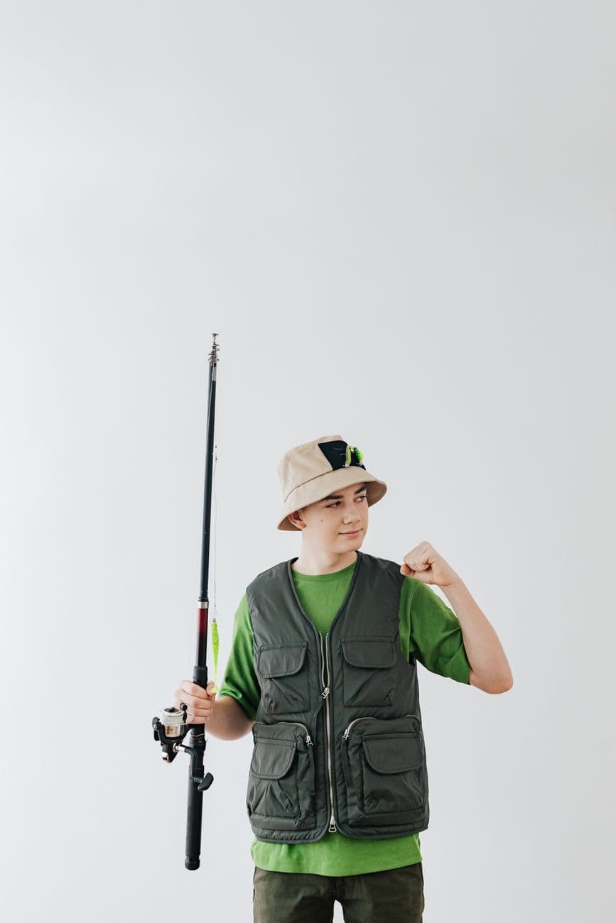Teenage boy in fishing attire posing with a fishing rod, showcasing leisure and hobby interest.