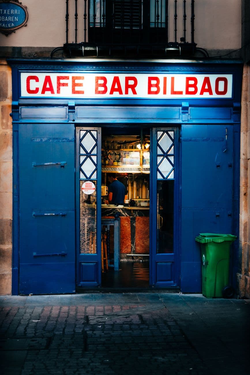 Inviting blue entrance of Cafe Bar Bilbao with warm interior lighting and urban appeal.