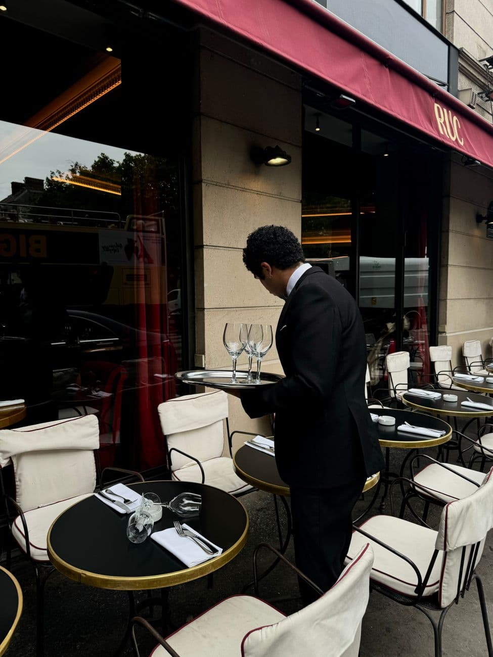 A waiter sets up tables at a stylish outdoor cafe with neatly arranged chairs and tables.
