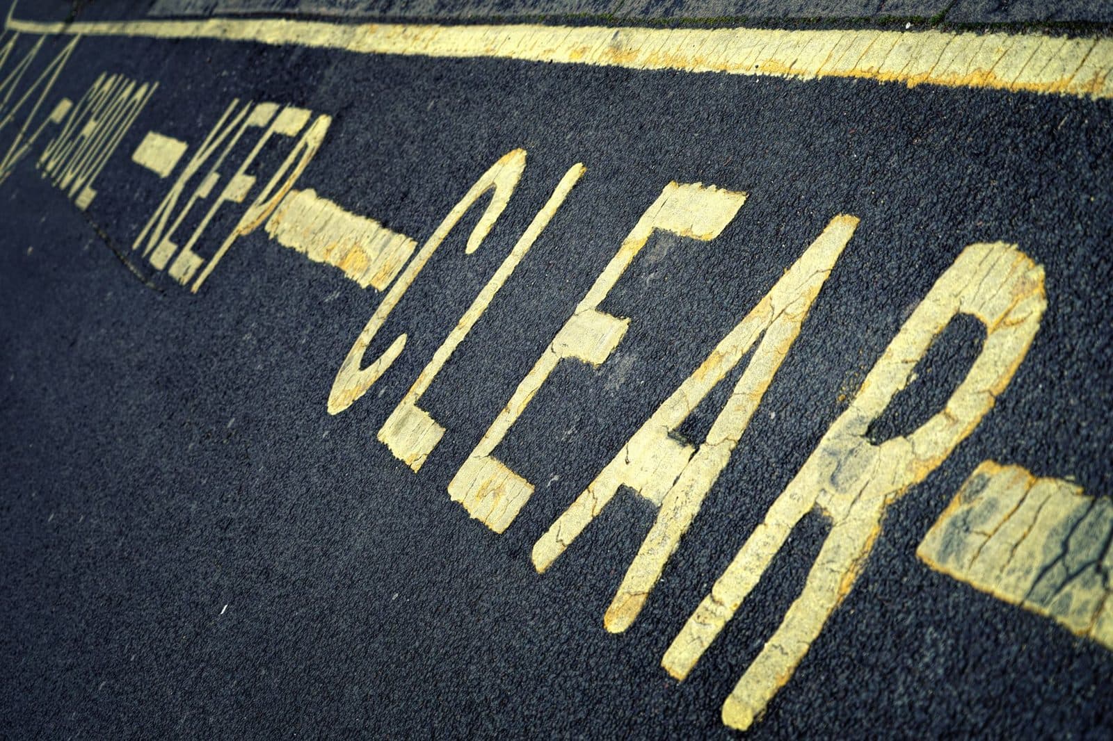 Close-up of yellow road markings with 'KEEP CLEAR' instruction on asphalt surface.