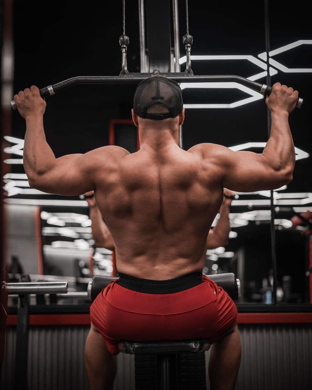 Muscular man performing lat pulldown exercise in a well-equipped gym.