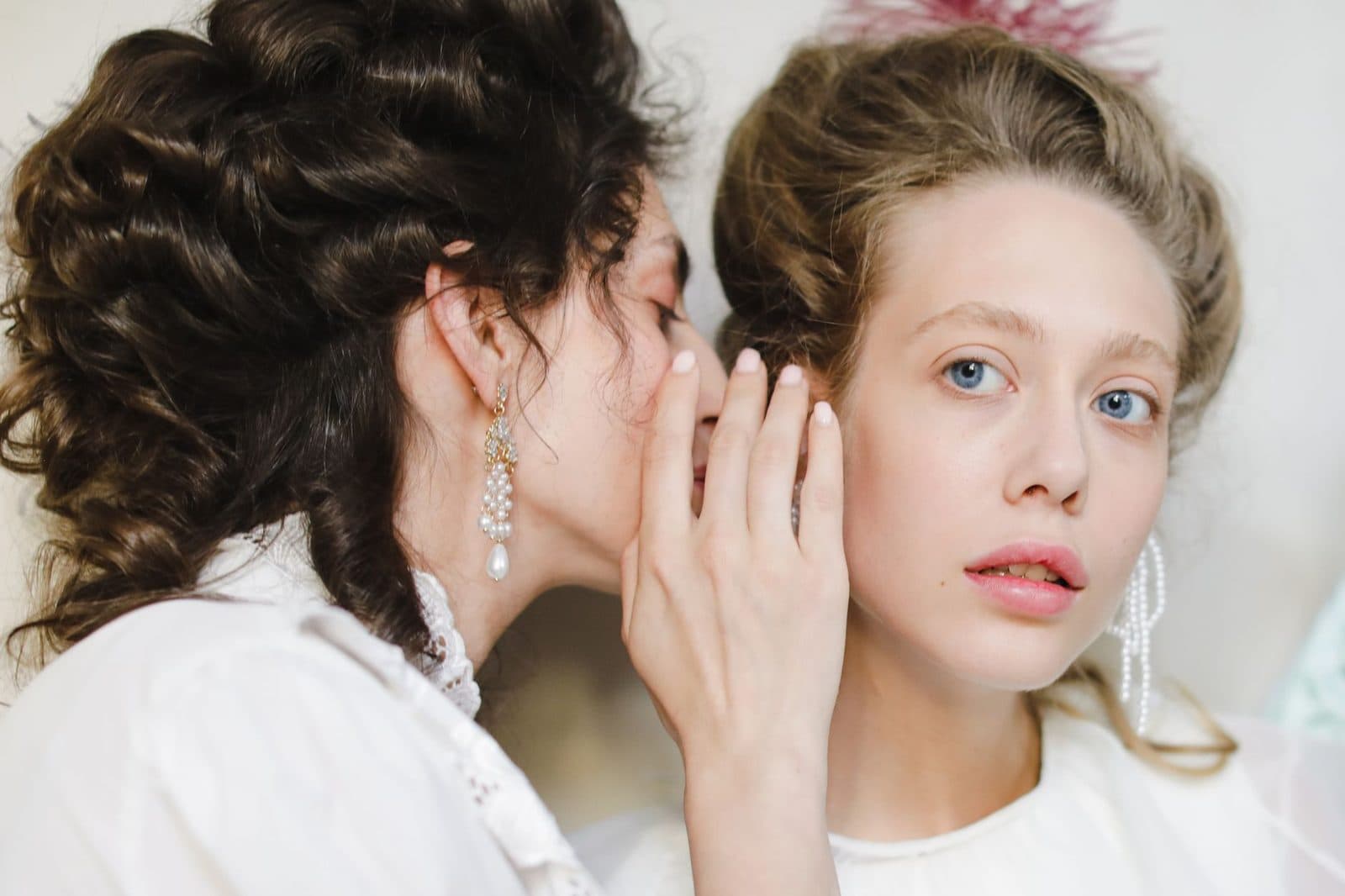 Two women dressed in 19th century fashion share a secret, showcasing elegance and friendship.