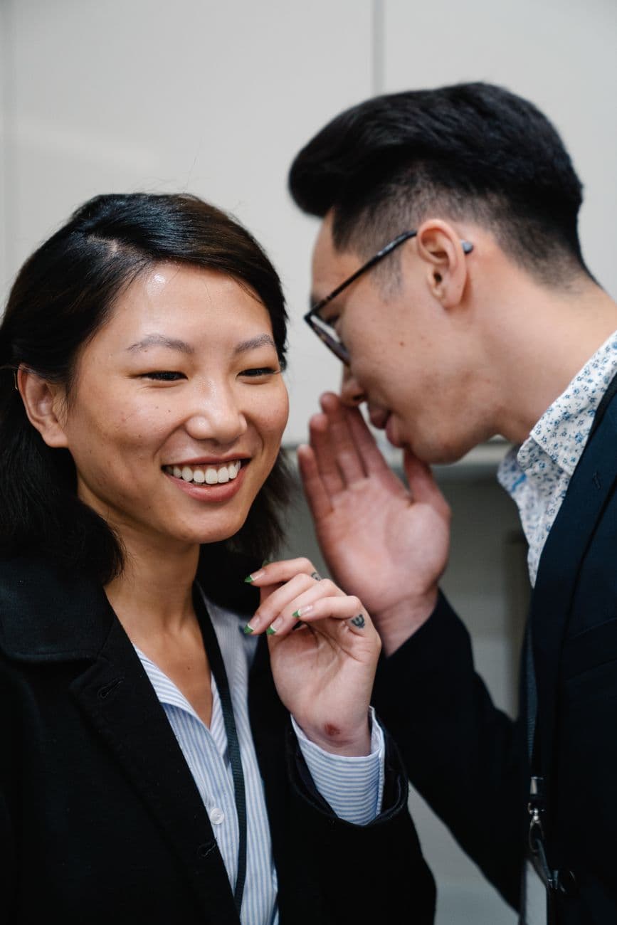 An Asian man and woman happily conversing, sharing secrets during office hours.