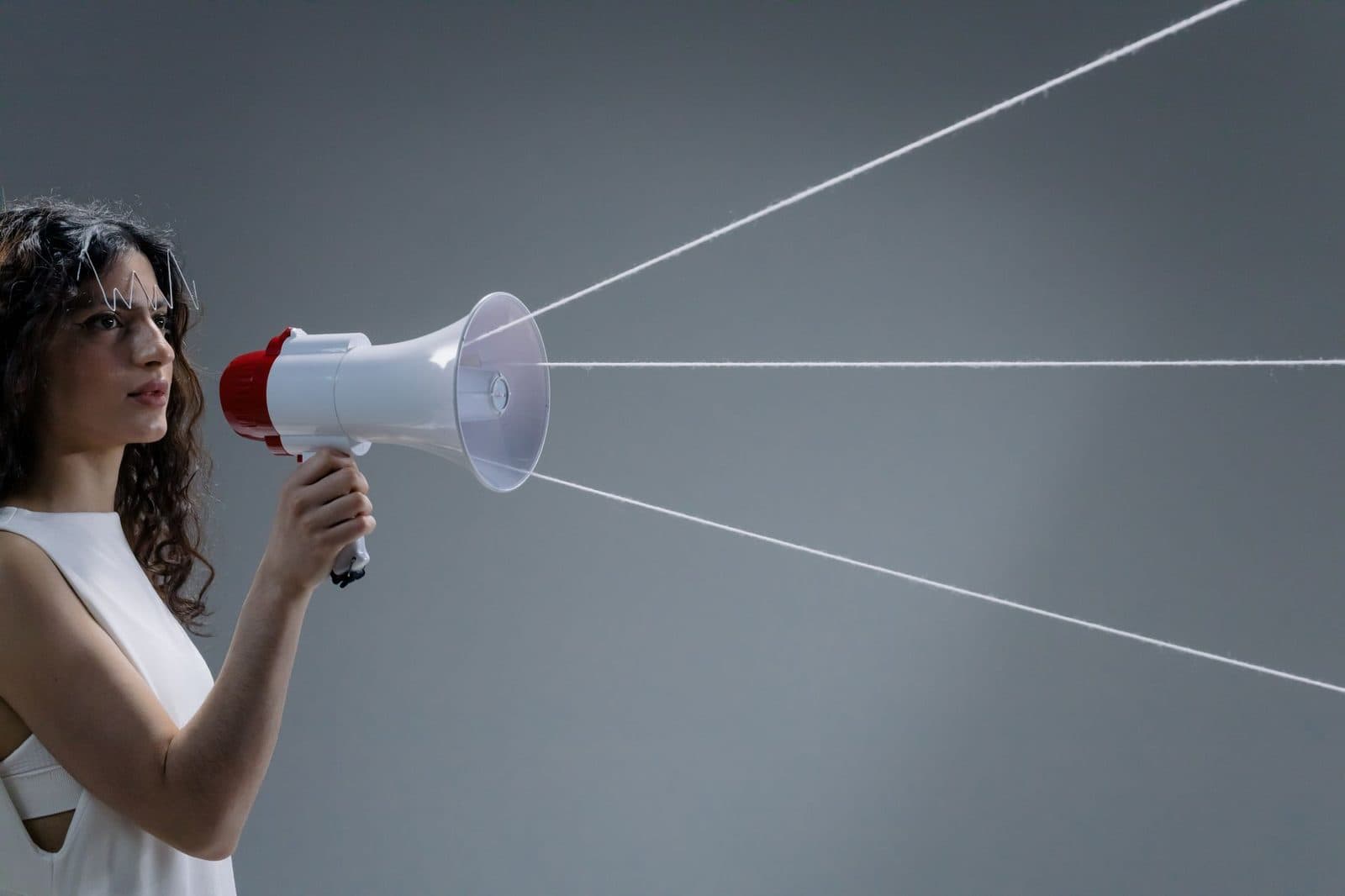 Young woman in a white tank top using a megaphone in a conceptual studio shoot.