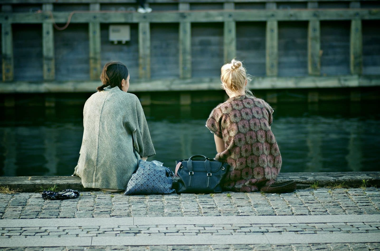 Two women sit along a canal in Copenhagen, Denmark, enjoying a serene moment by the water.