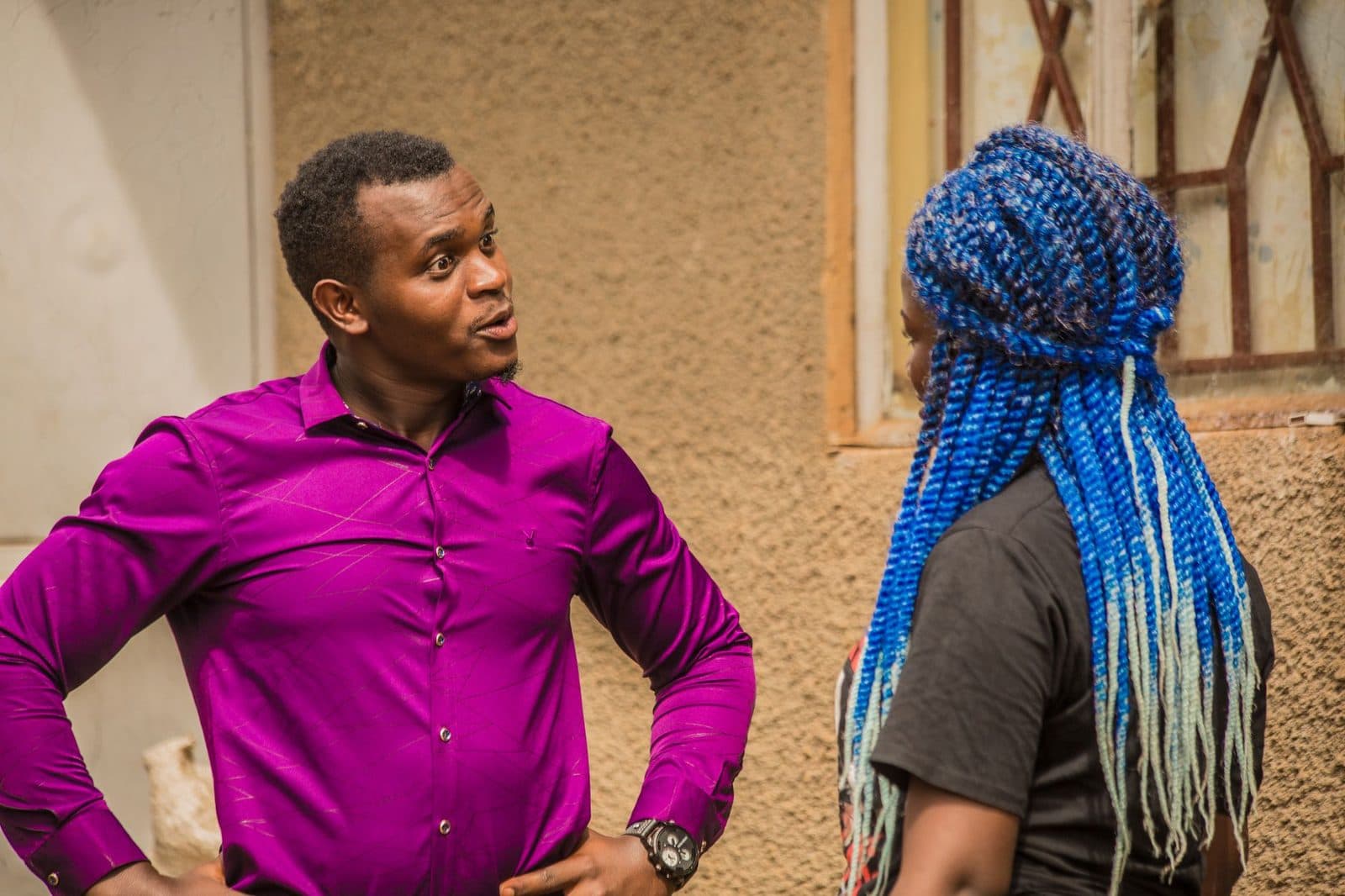 A man and woman conversing outside near a building facade in Uganda.