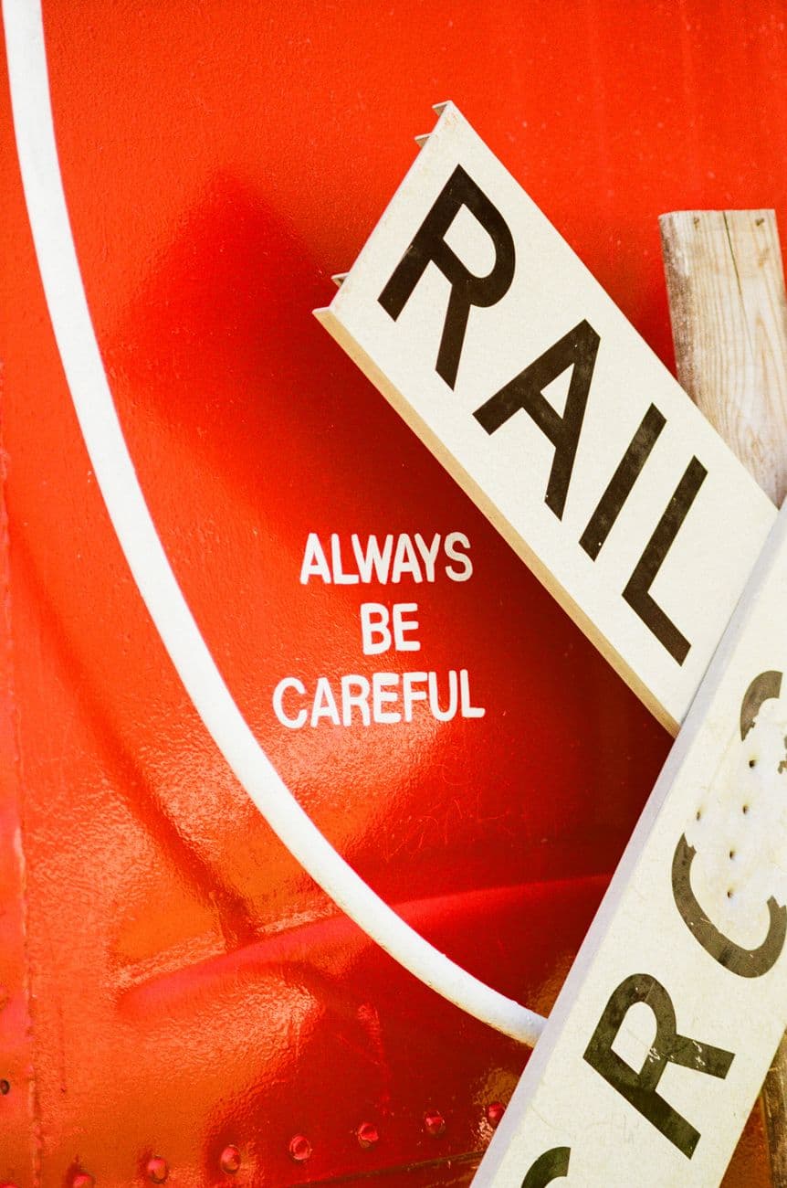 Close-up of a vibrant red railroad sign with 'Always Be Careful' message.